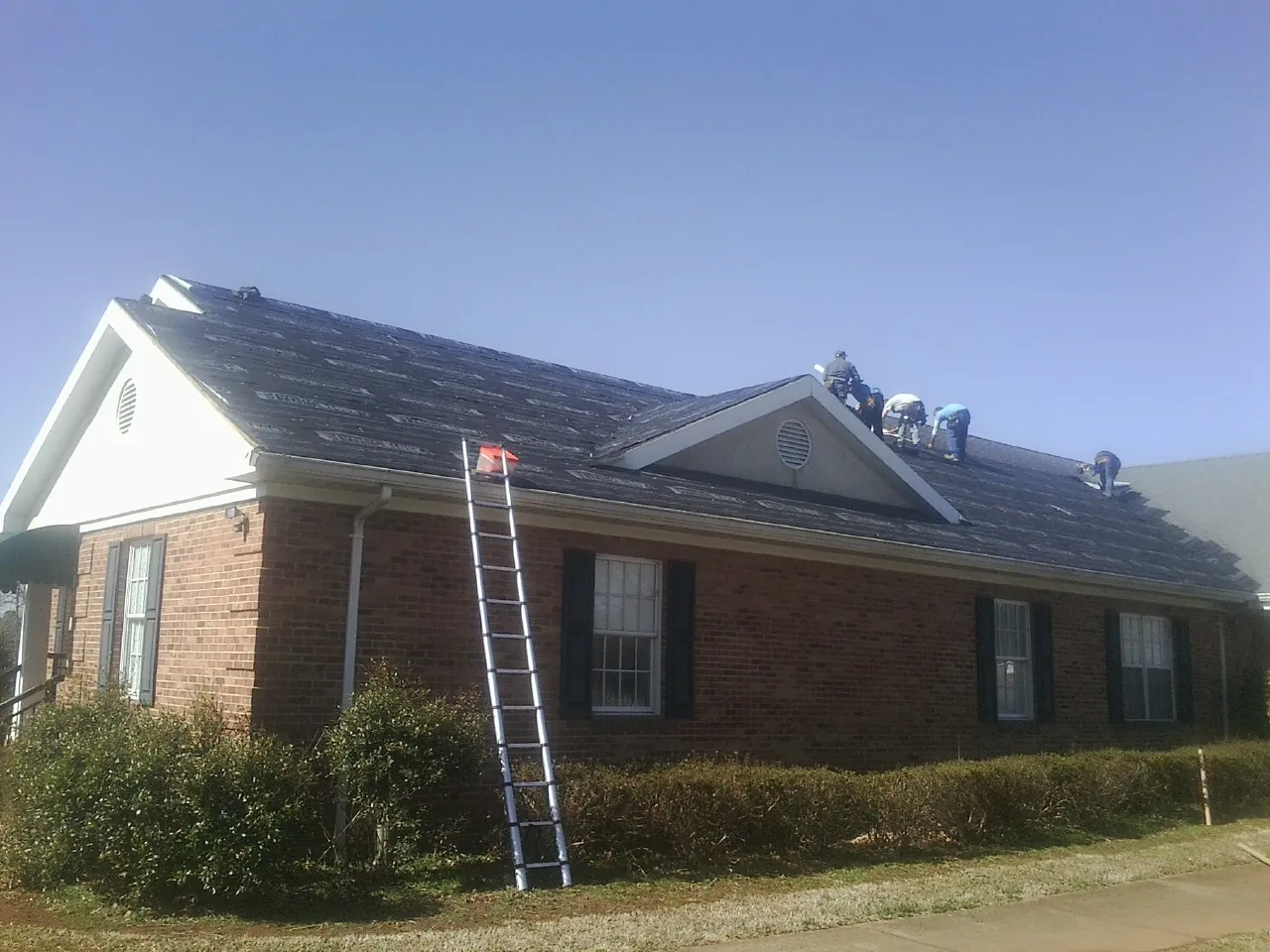 Crew tearing shingles off a brick ranch roof with a ladder set — Emergency Roof Repair work by our crew in Darragh