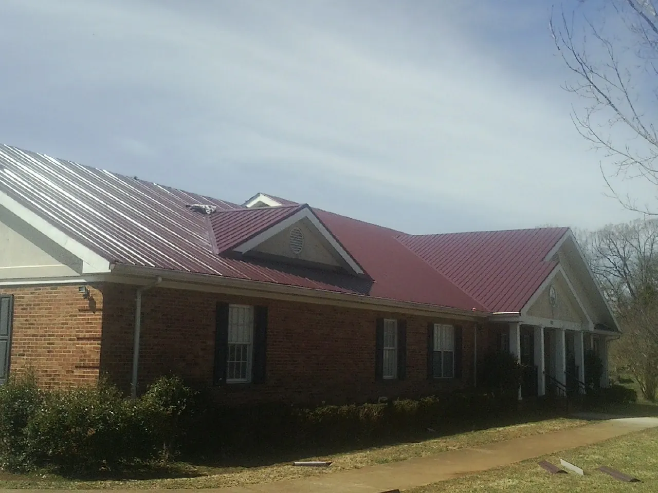 Red metal roof with gabled entries on a long brick building, from a Hail Damage Roof Repair job in Darragh
