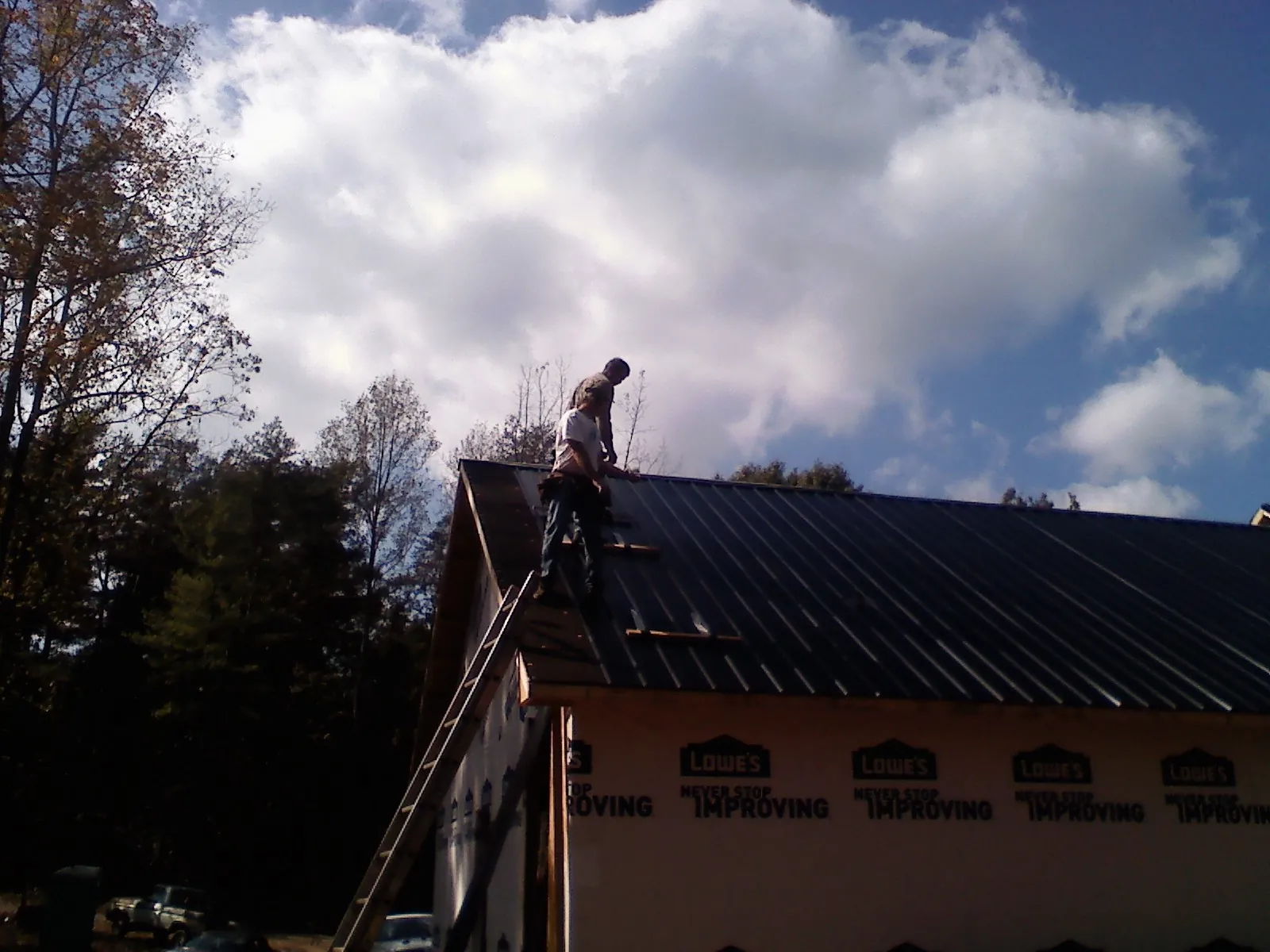 Roofer fastening dark metal panels high against a cloudy sky, from a Roof Inspection job in Darragh