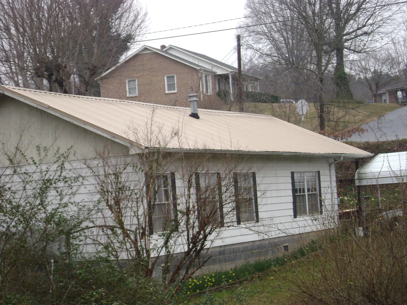 Tan metal roof on a white sided house set into a hillside — Commercial Roofing by Roofing Brothers in Darragh