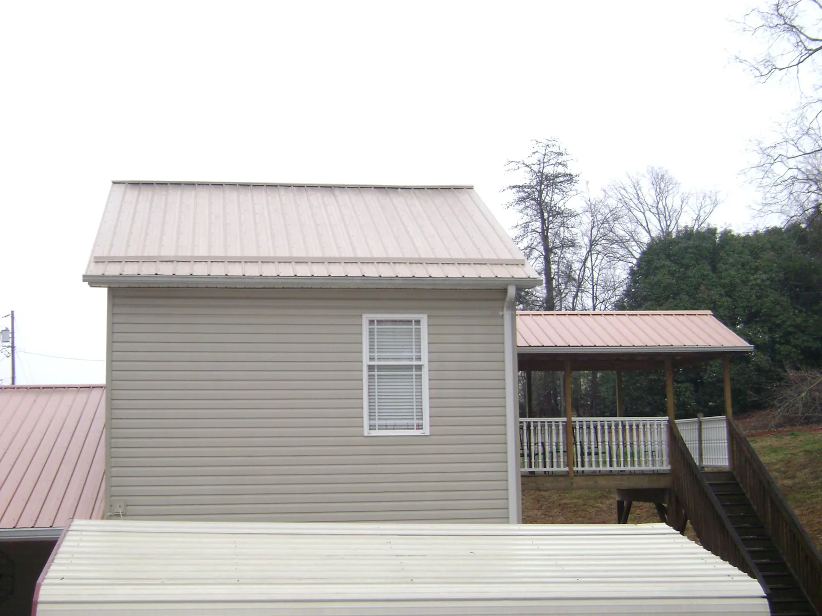 Tan metal roofs on a two story addition and attached porch, from a Roof Replacement job in Darragh
